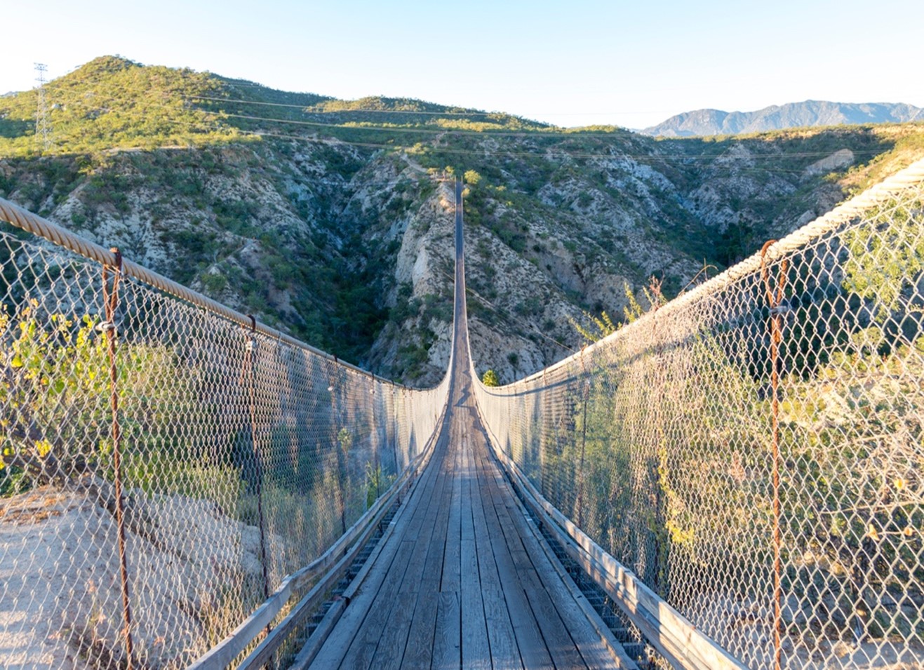 Image of a suspension bridge stretching over a wide canyon and into the distant green hills.