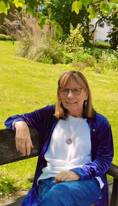 A photo of the author, Lynn Watson, sitting on a park bench in the sunshine